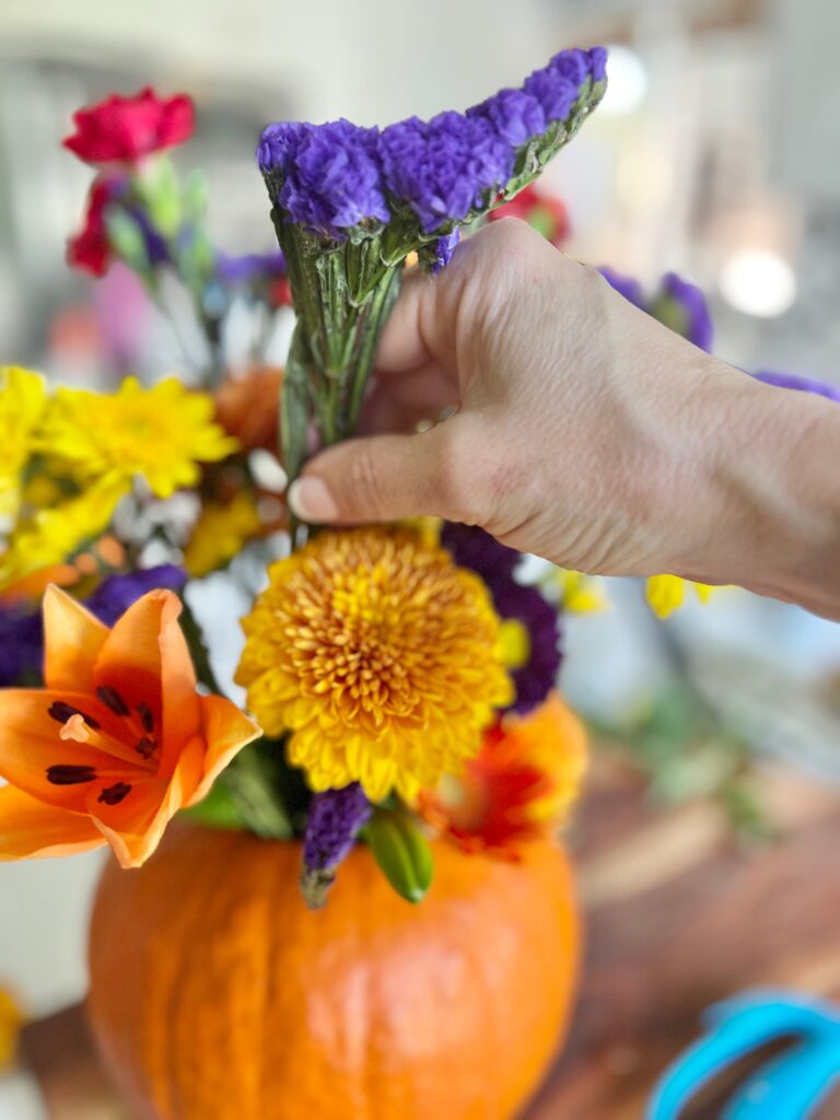 Arranging a purple flower for  pumpkin floral vase arrangements.