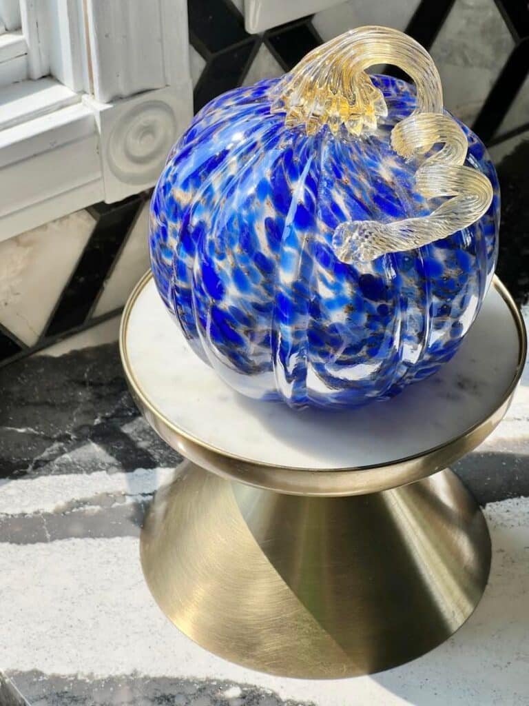A blue glass pumpkin sitting in front of a kitchen window.