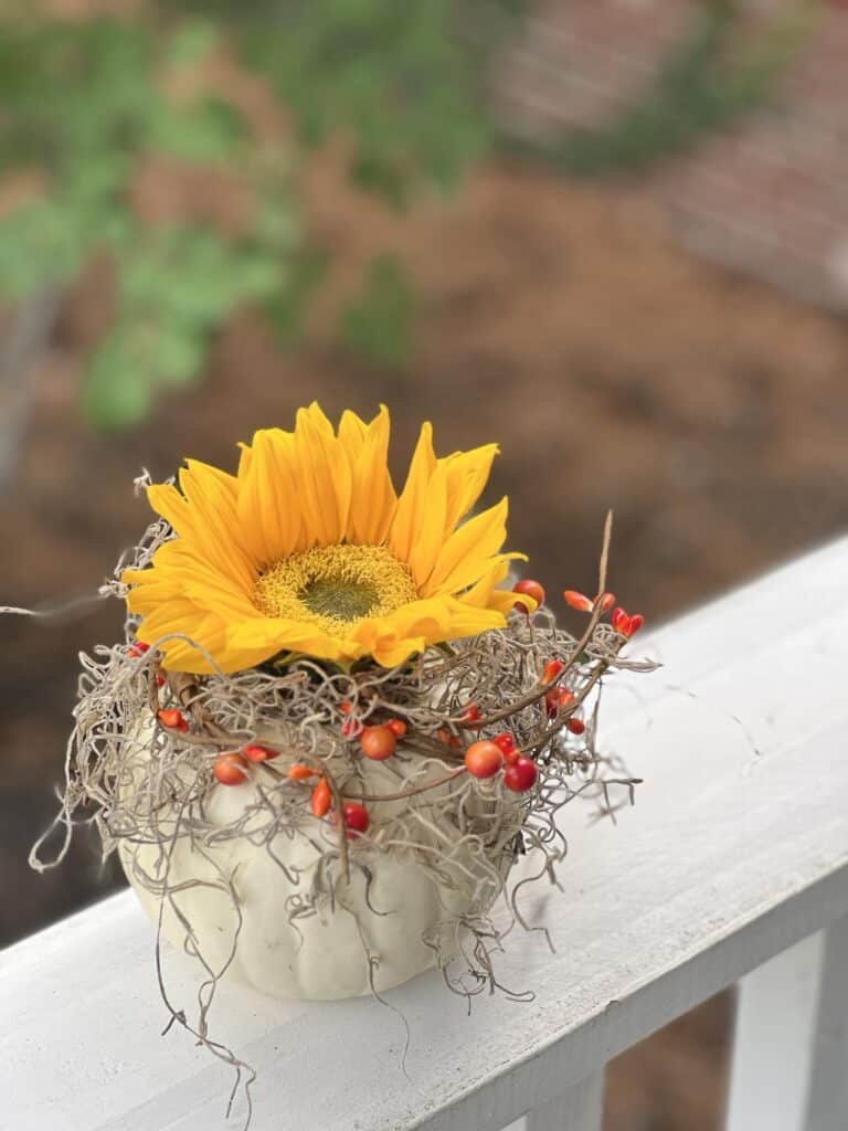 A sunflower pumpkin floral arrangement sitting on a porch railing.