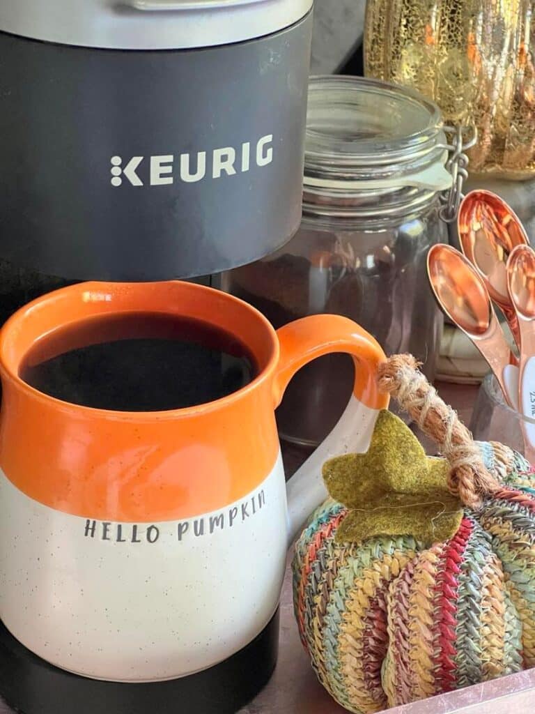 kitchen fall decor ideas: A large mug with the phrase "Hello Pumpkin" filled with coffee and sitting beside a woven faux pumpkin.