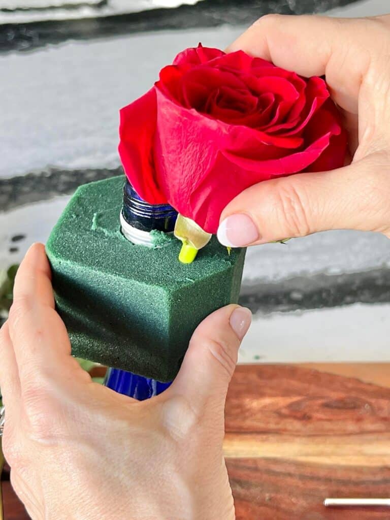 Inserting a red rose into the floral foam.