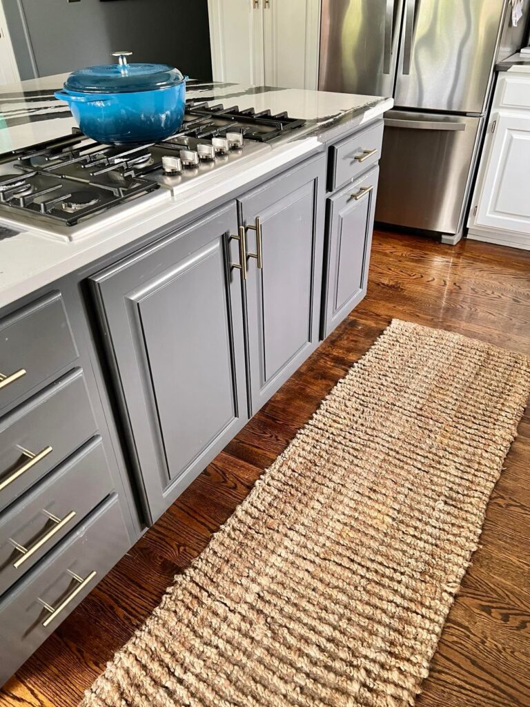 how to clean a jute rug: a jute rug runner laying on the floor in front of a kitchen island.