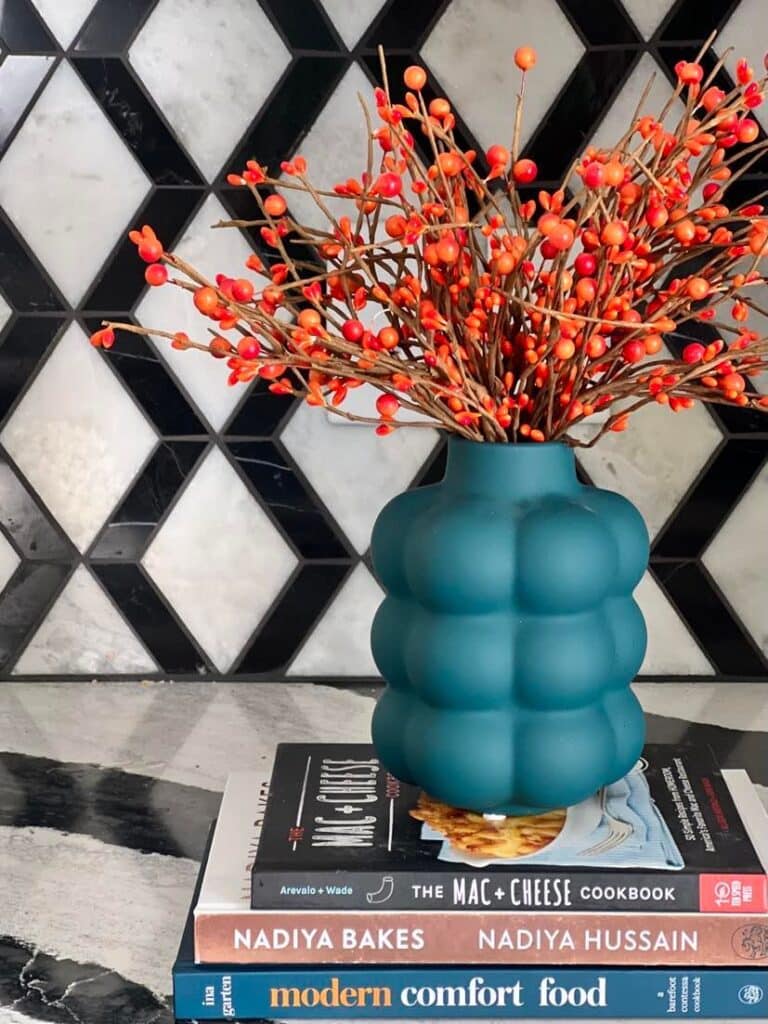 Orange pip berries in a blue vase sitting on top of stacked cookbooks is used as kitchen fall decor ideas.