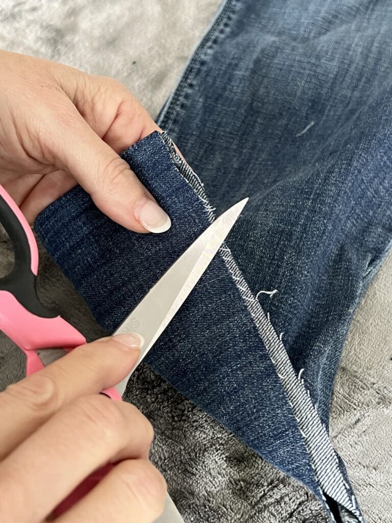 how to fray jeans: Using scissors blades to run across the hem fabric.