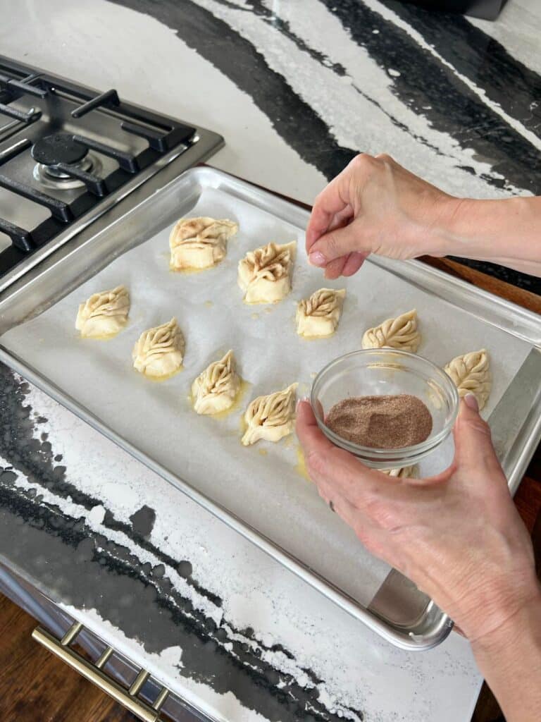 Sprinkling leaf shaped cookies with cinnamon sugar.