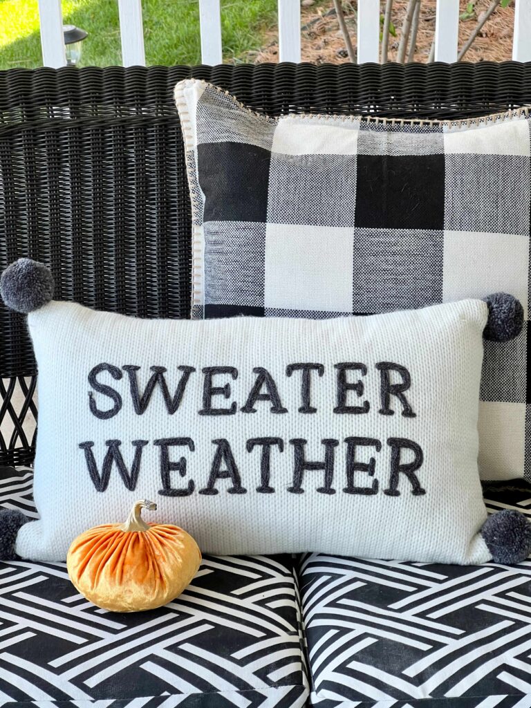 fall front porch decorating ideas on a budget: A pillow that says "Sweter Weather" on the front.