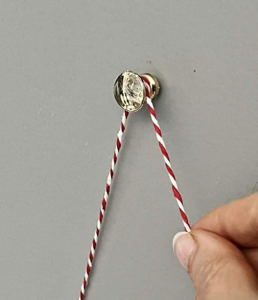 A thumbtack pressed into the wall with read and white twine wrapped around it.
