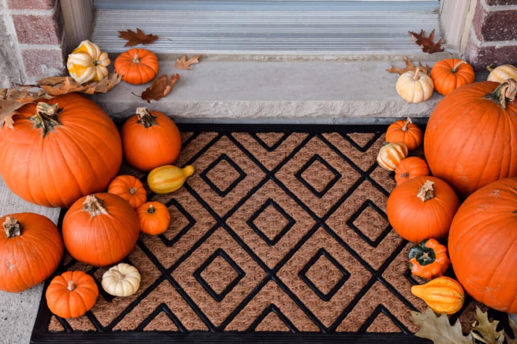 Orange pumpkins surrounding a door mat.