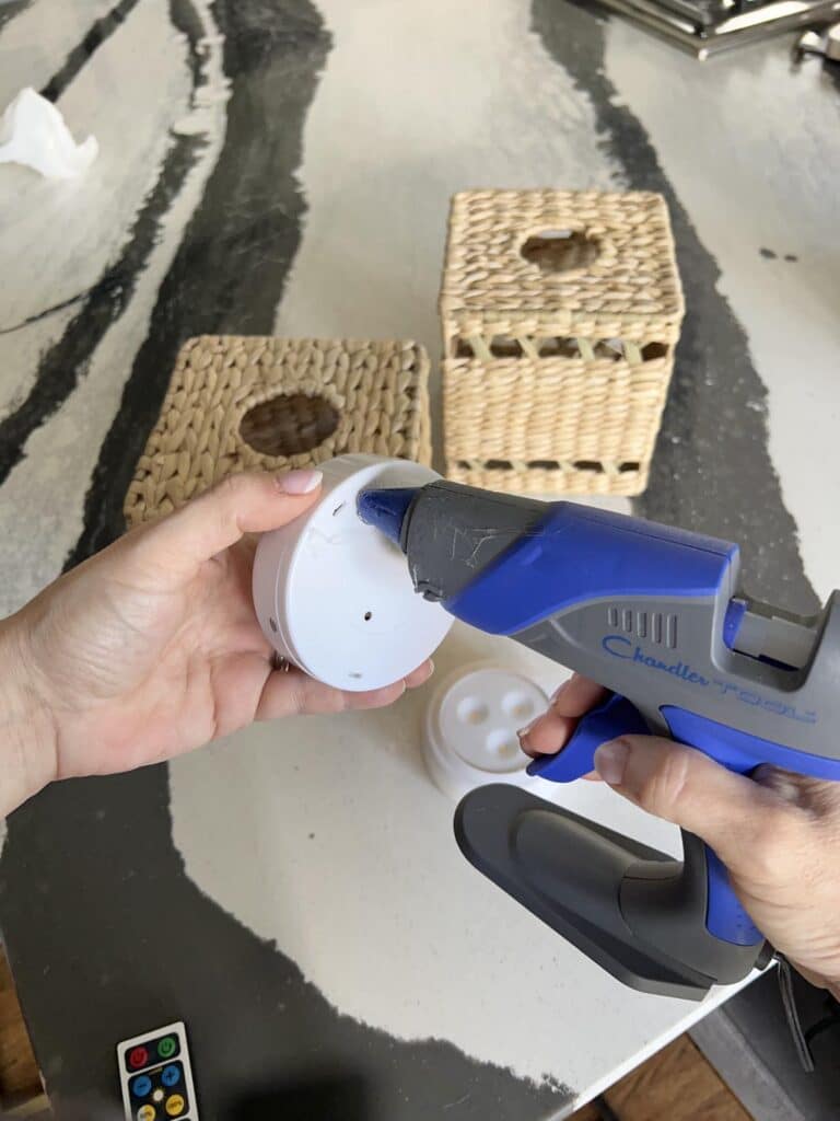 Applying hot glue to the back of a LED puck light.