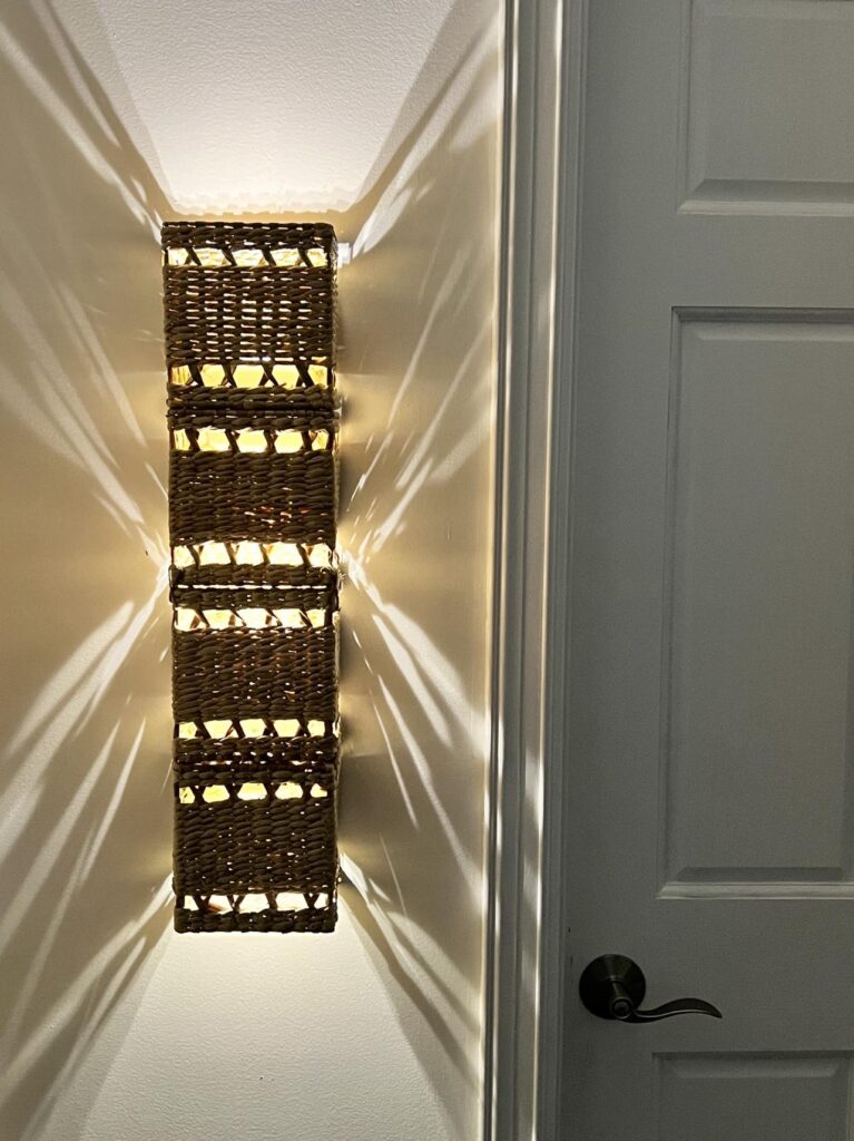 An illuminated rattan diy wireless wall sconce hanging in a hallway.