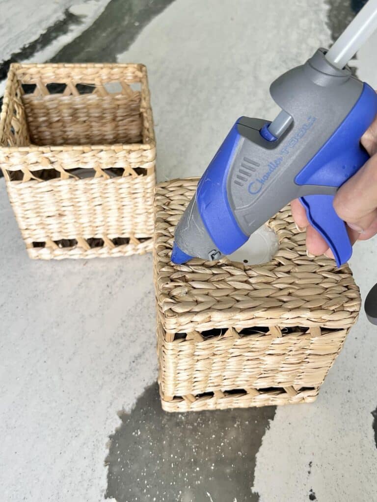 Applying hot glue to the top of a rattan tissue box.