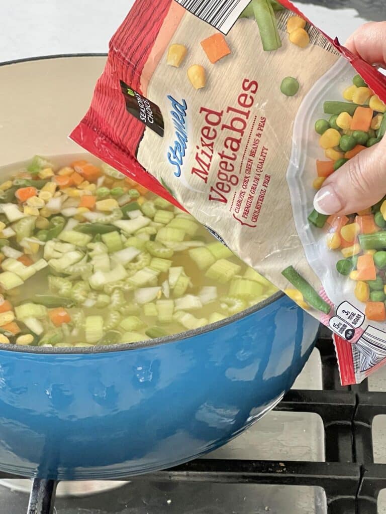 Pouring frozen mixed vegetables into a pot of brown jug cheese potato soup.