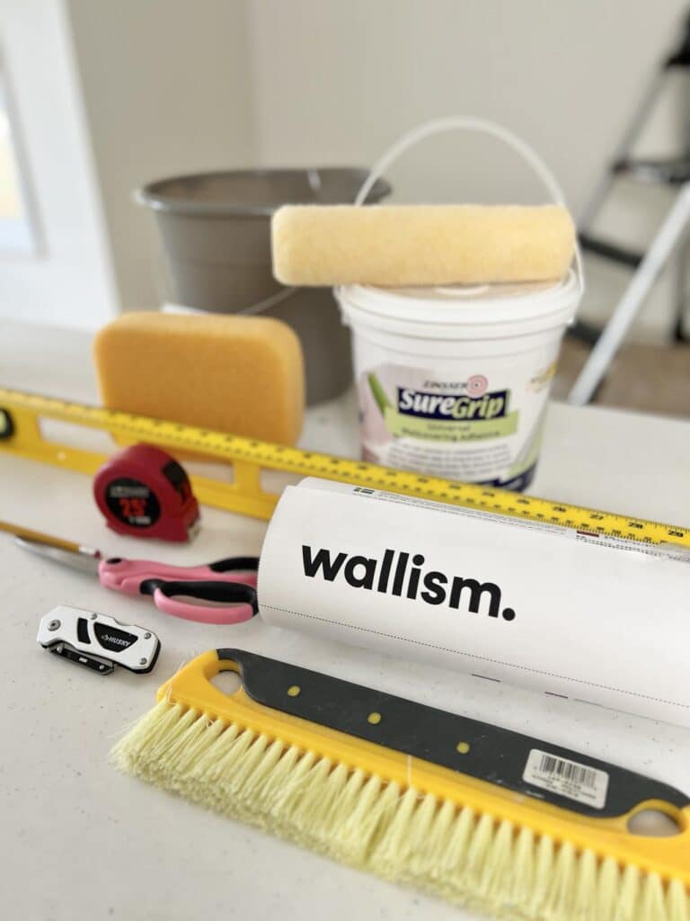 The supplies needed when you learn how to hang a wallpaper mural including wallpaper adhesive, a wallpaper brush, and a level.