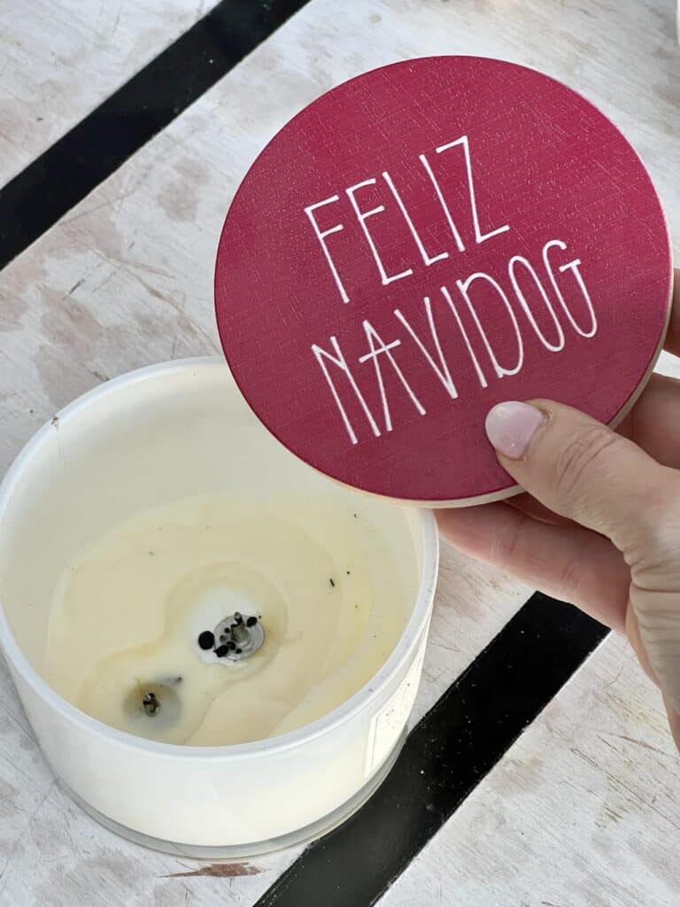 A whimsical wood candle jar lid witth the phrawse "feliz navidog " written on top.