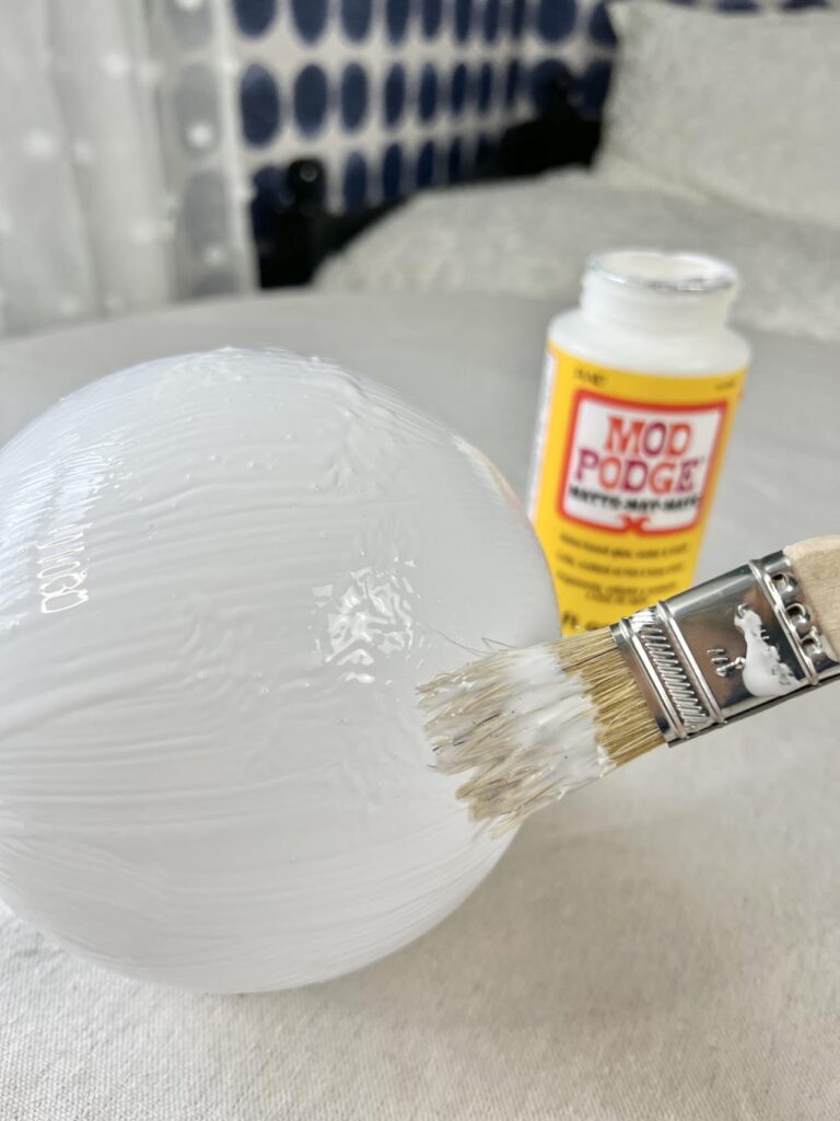 Applying mod podge to a glass globe.