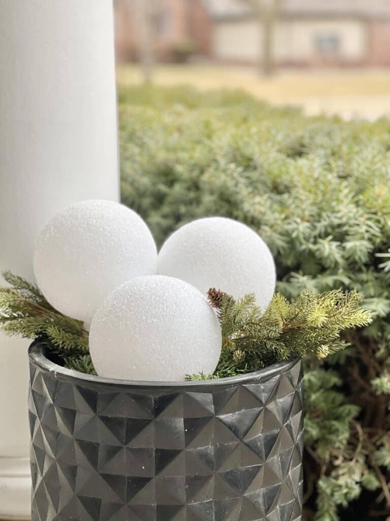 diy faux snowballs placed in a garden pot on the front porch.