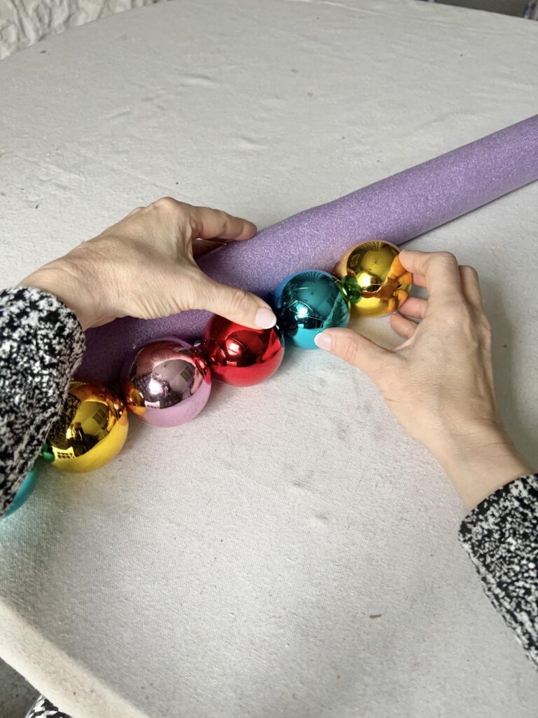 Gluing Christmas ball ornaments to the perimeter of a pool noodle.