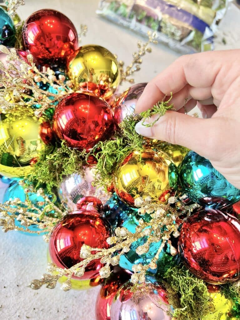 Tucking green moss into the spaces between Christmas ball ornaments.