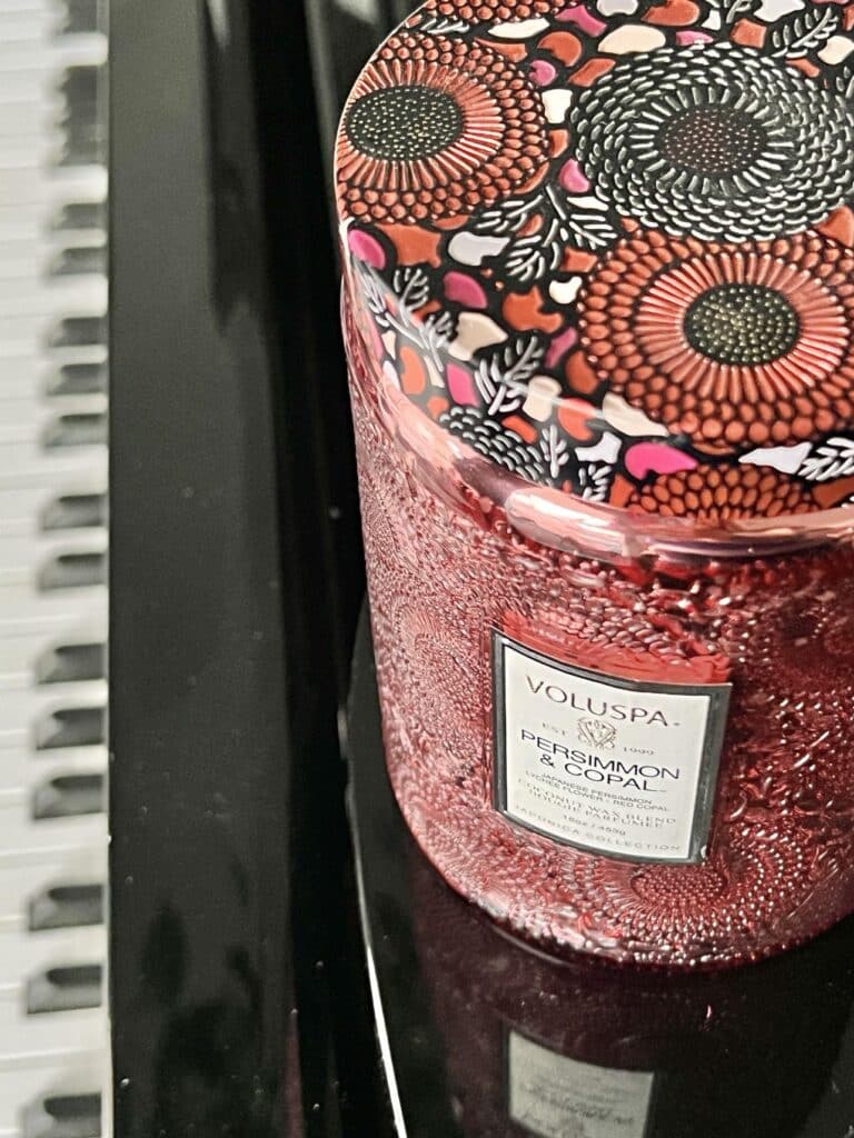 A candle jar with a lid sitting on top of a piano.