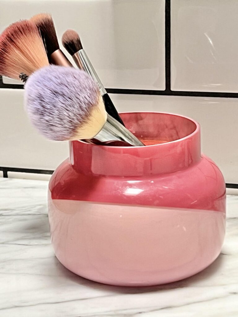 A pink candle jar holding makeup brushes.