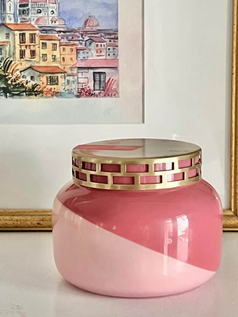 A pink candle jar sitting on a shelf in front of some propped artwork.