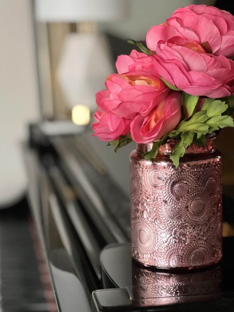 A candle jar holding faux flowers and sitting on a piano.