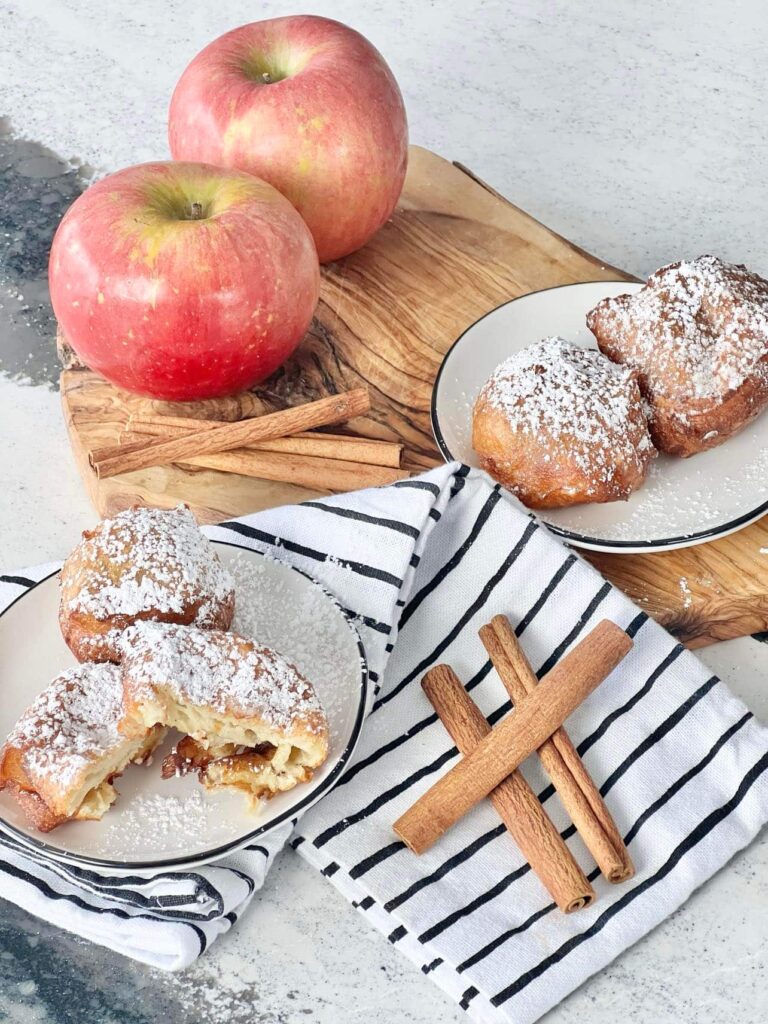 Two apples sitting besides plates holding apple beignets.