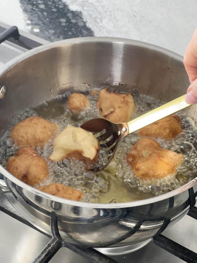 Flipping apple beignets in the hot oil as they brown.