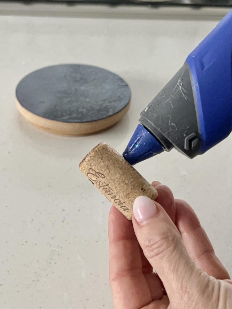 Hot glueing a used wine cork to the top of the wood candle jar lid to repurpose the candle jar as a tea caddy.