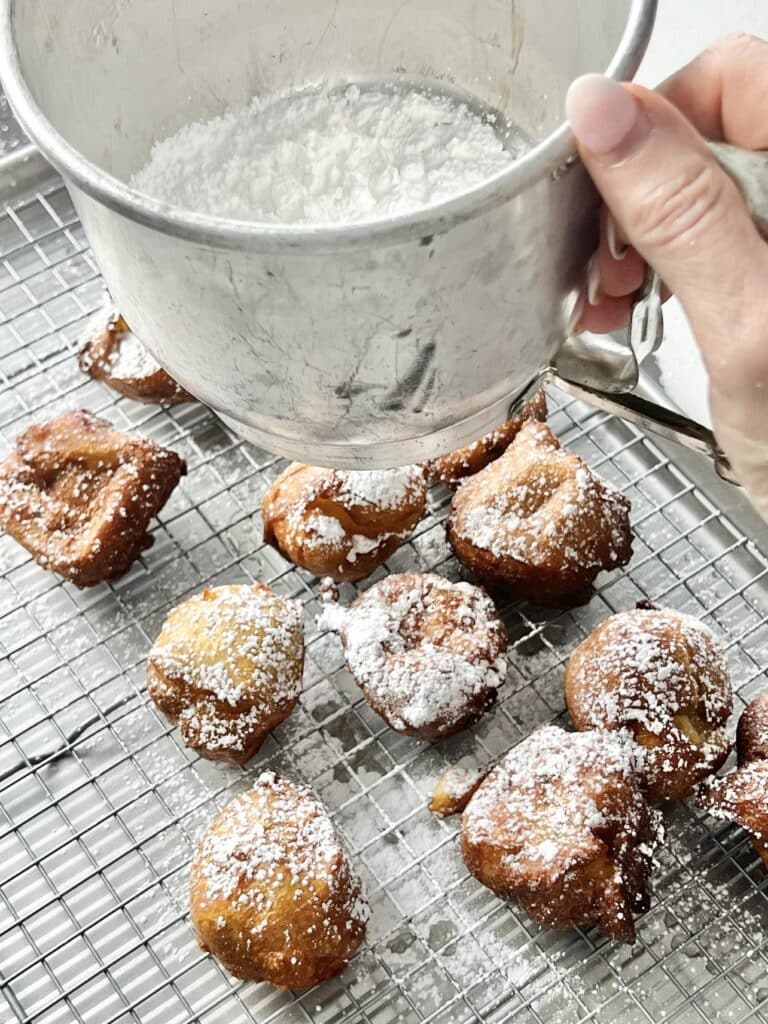 Sifting powdered sugar on top of fried apple beignets.