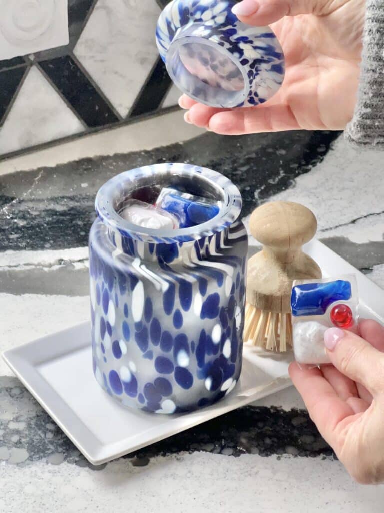 Placing dishwasher tabs for storage in a glass candle jar container.