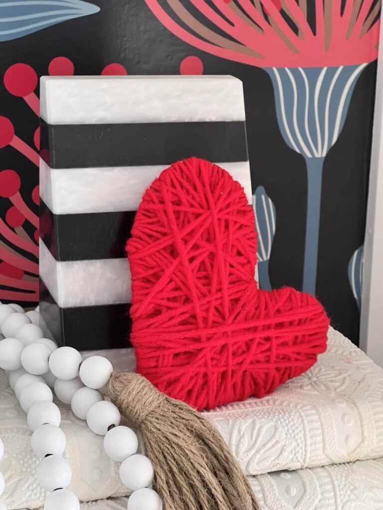 A wood bead garland nestled beside a red yarn heart. How to decorate with bead garland for the holidays.