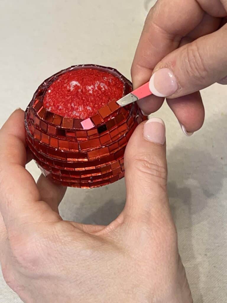 Applying tiles to the DIY Disco Ball Cherries with tweezers.