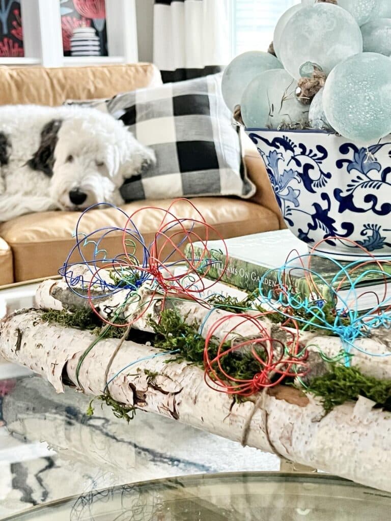 Decorated birch logs displayed on a coffee table with a dog looking on.