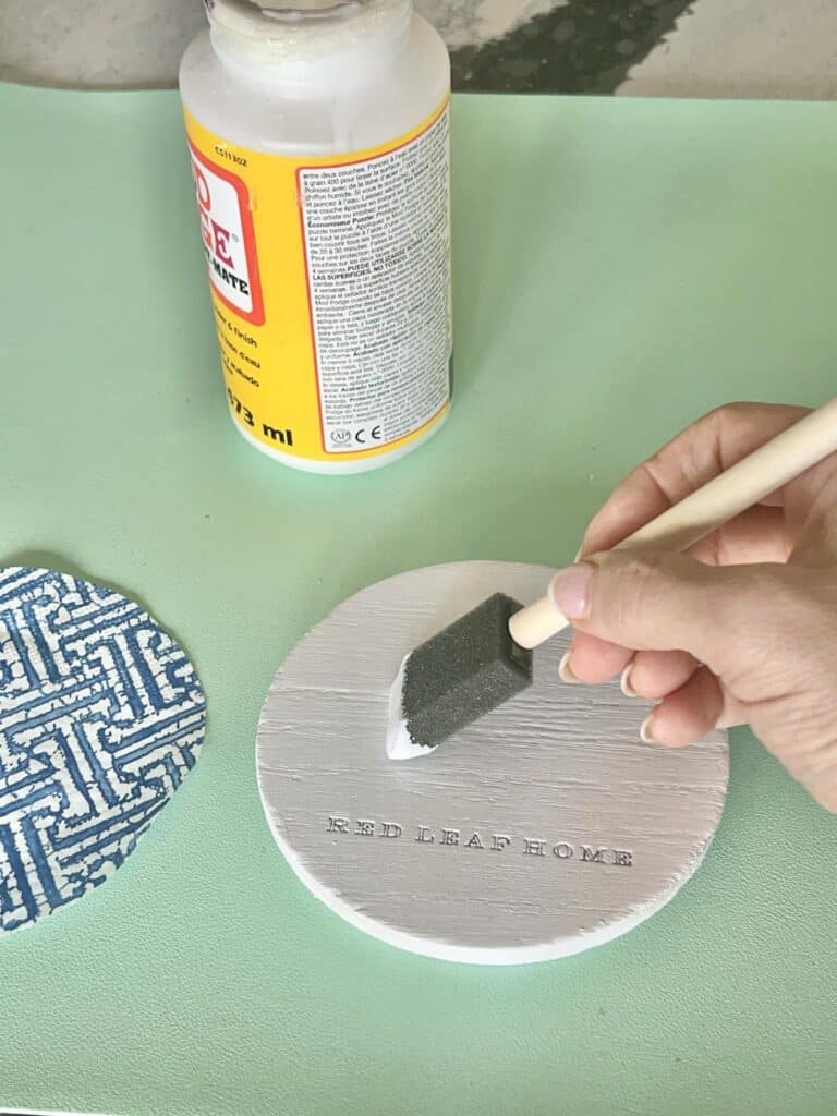 Brushing Mod Podge decoupage glue to the top of a painted candle jar lid.