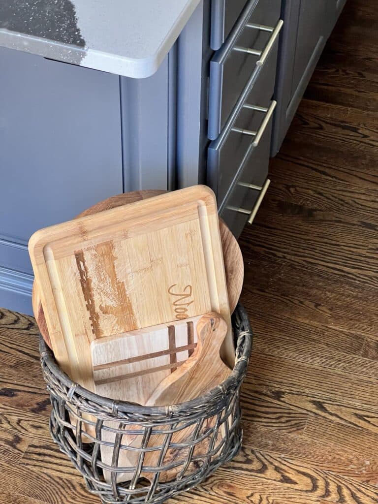 how to decorate a space with functionality  includes storing wooden cutting boards in a basket beside the kitchen island.