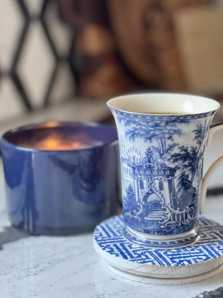 DIY Decoupage Coaster holding a cup of coffee and sitting beside a jar candle.