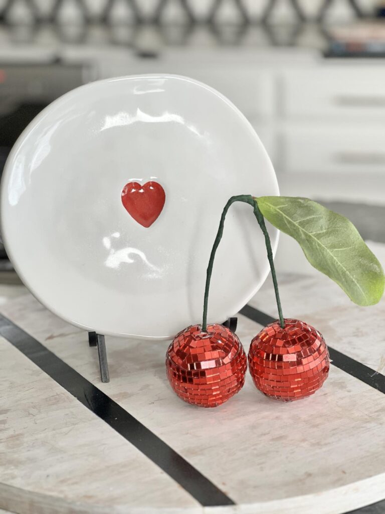 DIY Disco Ball Cherries sitting in front of a white plate with red heart.