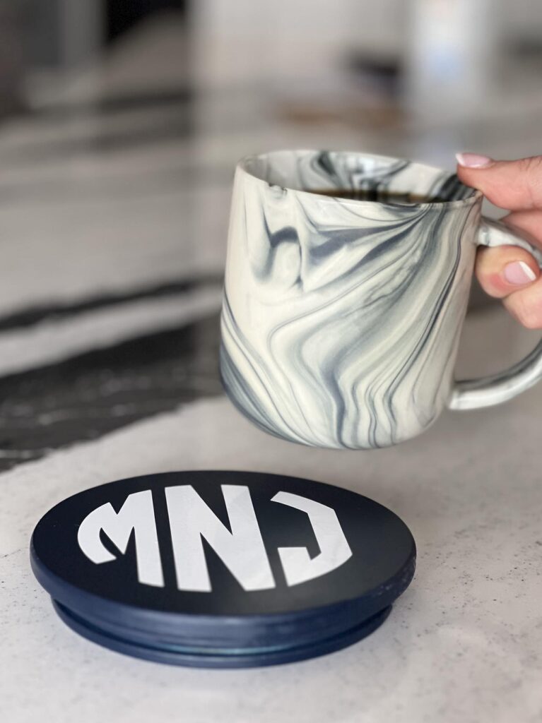 A cup of coffee being placed on a monogrammed candle lid coaster.