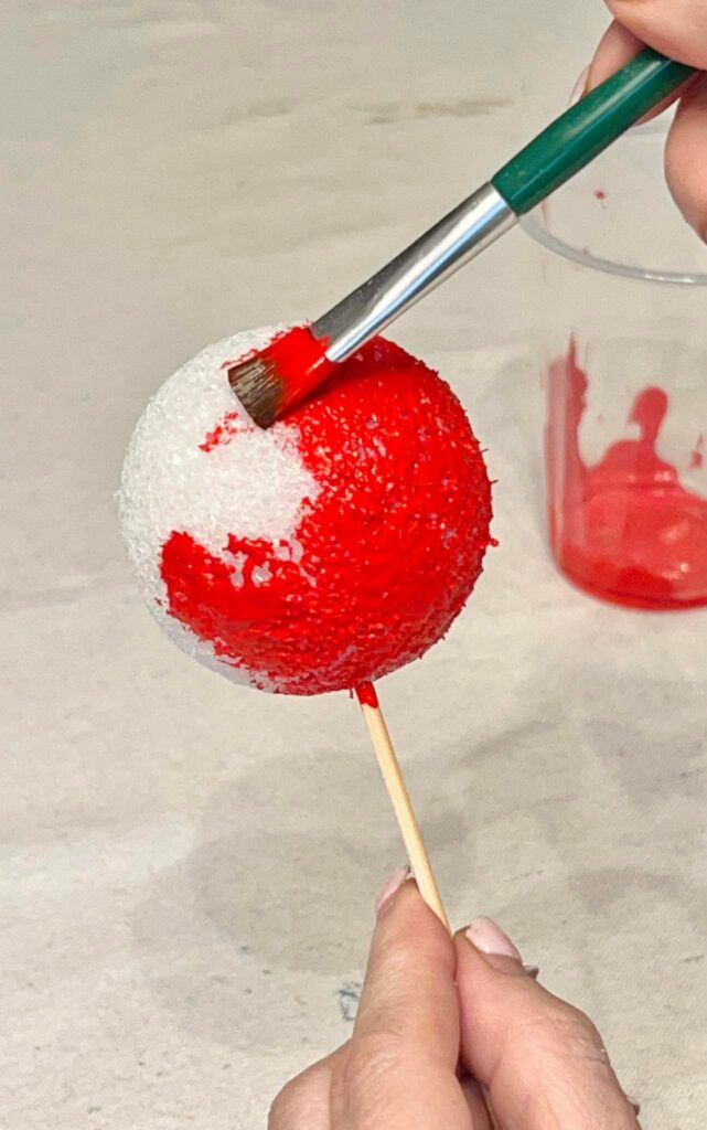 Painting a styrofoam ball with red paint.