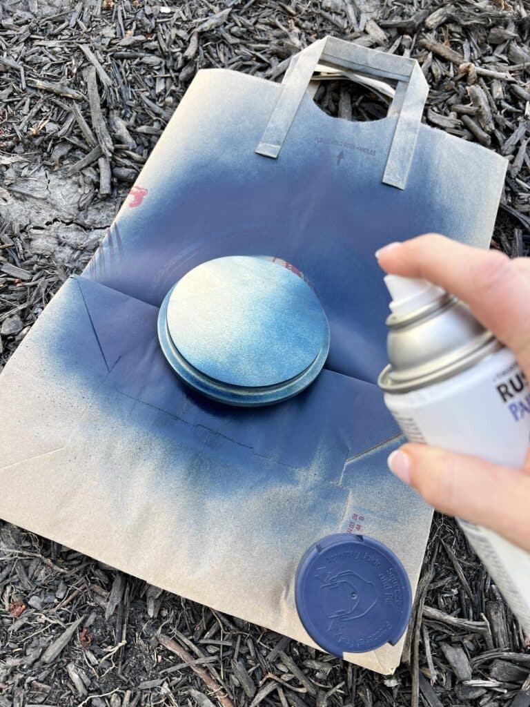 Spray painting a candle lid navy blue.