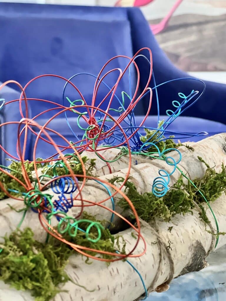 DIY Wired Flower Birch Logs placed in front of a cobalt blue chair.