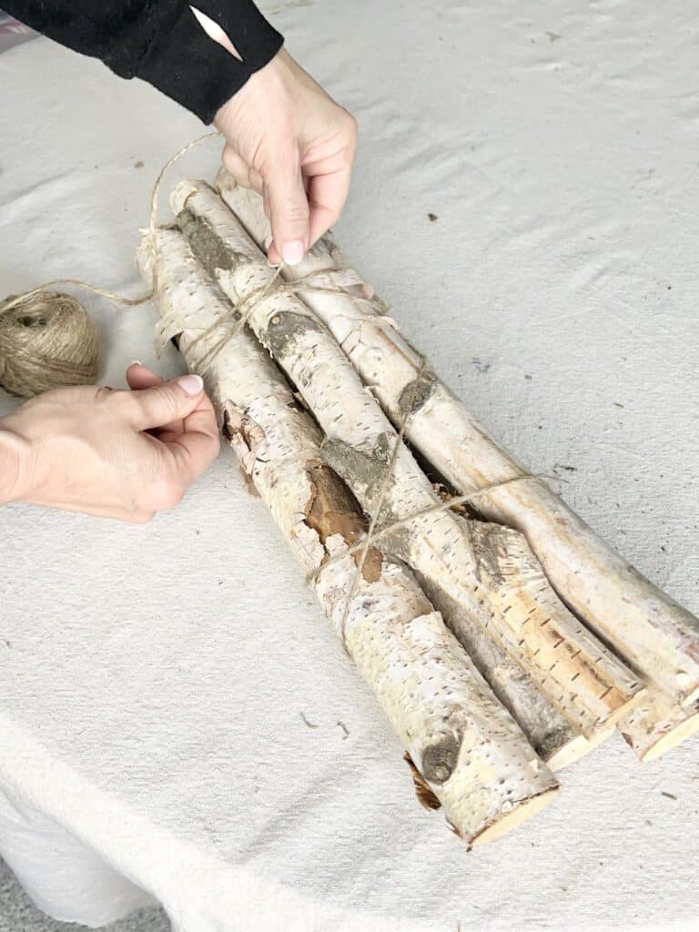Securing a bundle of birch logs with jute twine for this DIY project.