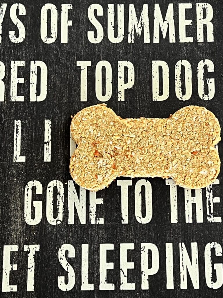 A homemade carrot oatmeal dog treat sitting on a wood board that says "Top Dog."