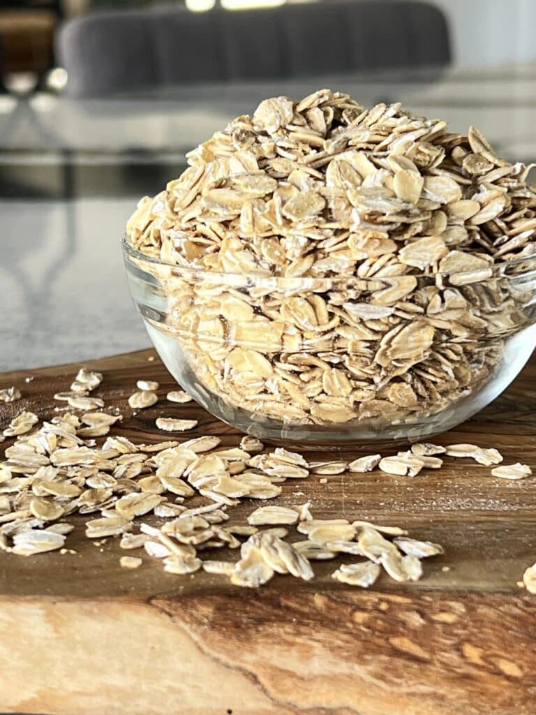 A bowl of rolled oats for homemade oatmeal dog treats sitting on a cutting board.