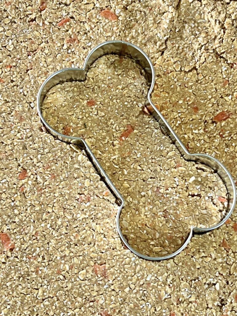 A dog-shaped cookie cutter pressed into rolled out dog treat dough.