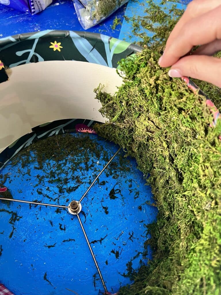 Pressing green moss onto the sticky inside of the lampshade.