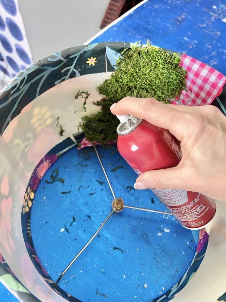 Spraying adhesive to the inside of the lampshade to create the inside of the DIY Door Wreath.