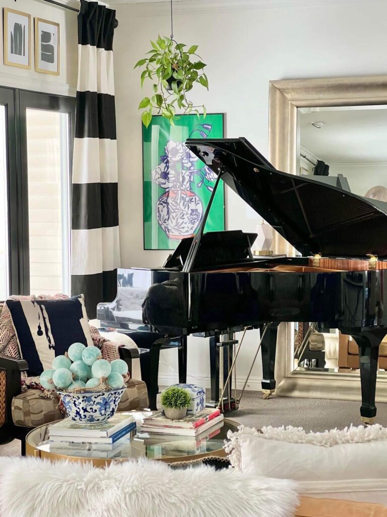 A shiny black baby grand piano surrounded by glamorous decorating ideas like bold wall art, oversized mirror, and textured bead garland.