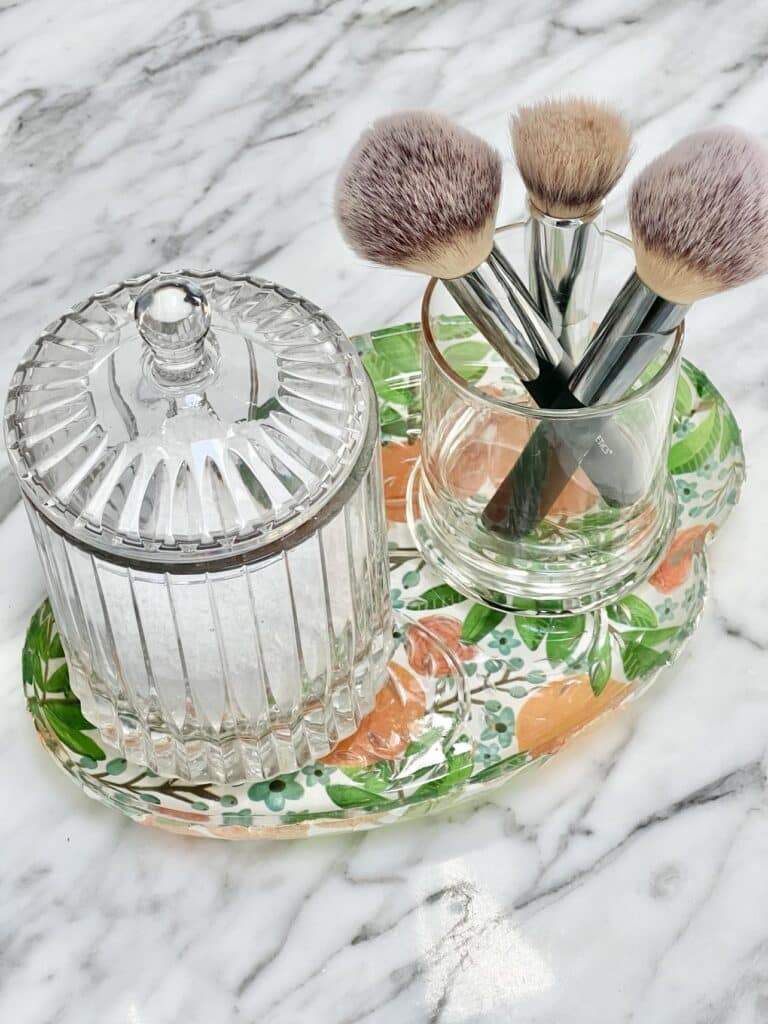 A decoupage glass plate used as a vanity tray holding makeup brushes.